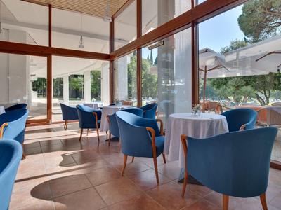 Helles Café mit großen Fenstern, blauen Stühlen und weißen Tischtüchern, sonnendurchflutet.