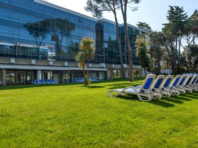 Grüne Wiese mit Reihen von blauen Liegestühlen und modernen Glasgebäuden im Hintergrund.