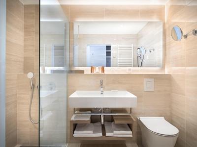 Modernes Badezimmer mit WC, Waschbecken, Spiegel, gefliesten Wänden und integrierter Dusche.