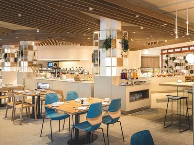 Área de restaurante de hotel moderna con sillas azules, mesas de madera y luz cálida.