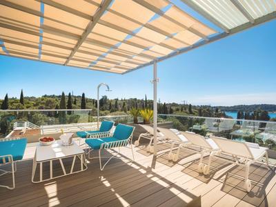Terraza con tumbonas y zona de estar con vista a una piscina soleada y colinas.