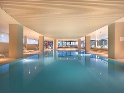 Piscina cubierta luminosa con diseño moderno, grandes ventanales y áreas de asiento.