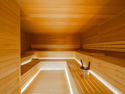 Helle Sauna aus Holz mit mehrstufigen Bänken und einem Eimer mit Aufgusskelle.