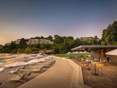 Resort mit Pool, Sonnenliegen, Sitzbereich und Hügel mit Villen bei Sonnenuntergang.
