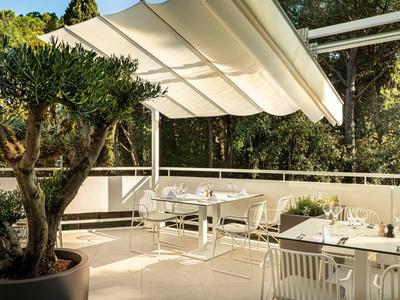 Helle Terrasse mit weißen Möbeln, großen Pflanzkübeln und ausfahrbarer Markise im Sonnenschein.