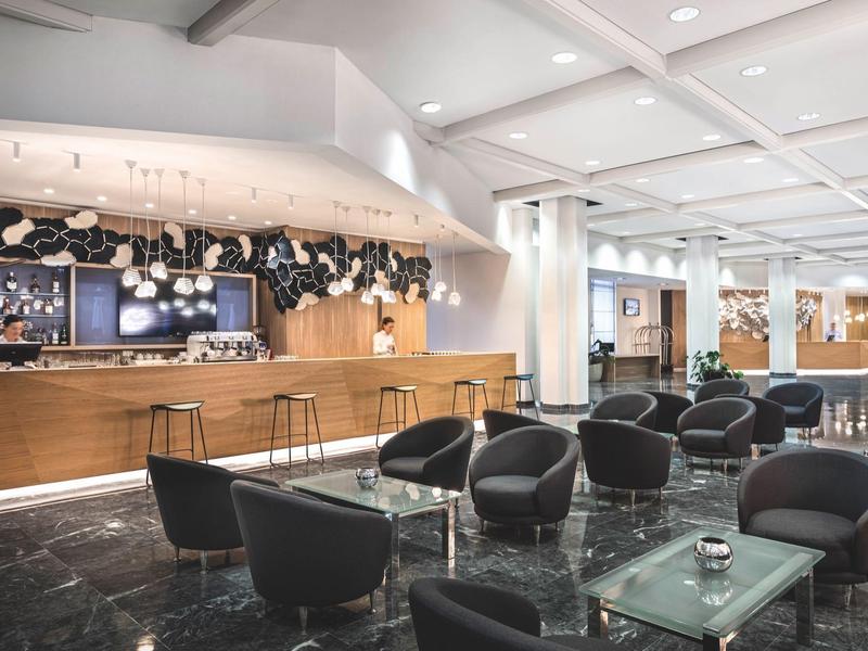 Moderner Lounge-Bereich mit schwarzen Sesseln, Glastischen und Holzbar in hellem Raum.