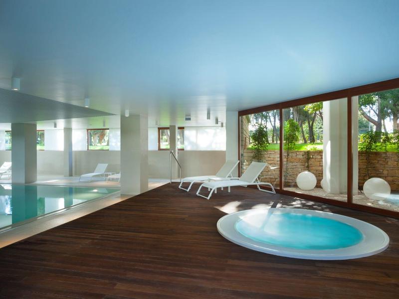 Moderner Spa-Raum mit Innenpool, Whirlwanne, Holzfußboden und Liegestühlen am Fenster.