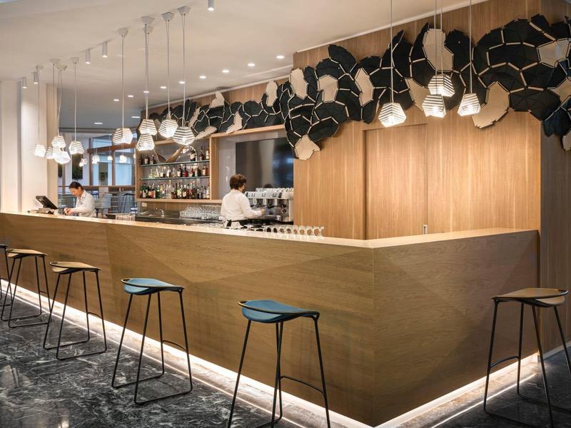 Moderner Barbereich mit langen Holztheken, schwarzen Barhockern und dekorativen Pendelleuchten.