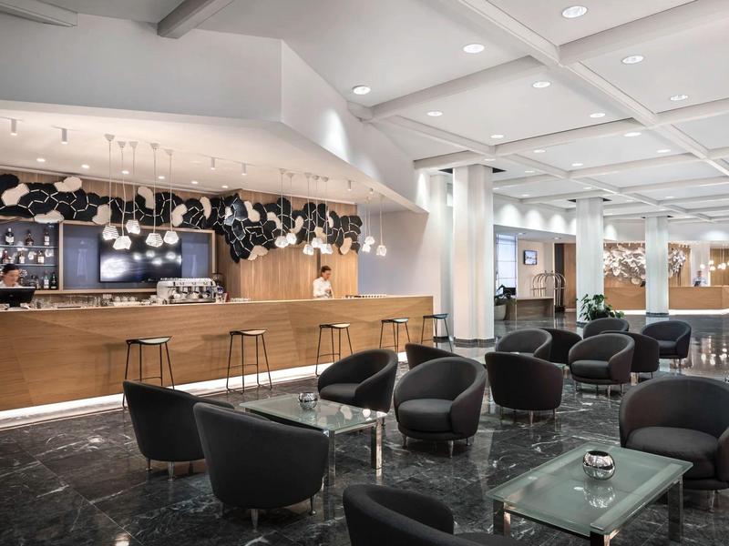 Moderner Lounge-Bereich mit schwarzen Sesseln, Glastischen und Holzbar in hellem, offenem Raum.