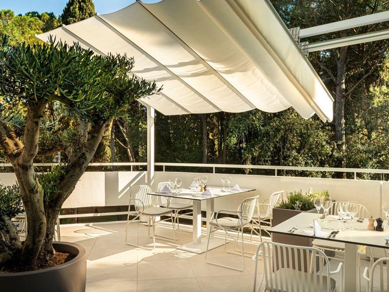 Helle Terrasse mit weißen Möbeln, großen Pflanzkübeln und ausfahrbarer Markise im Sonnenschein.