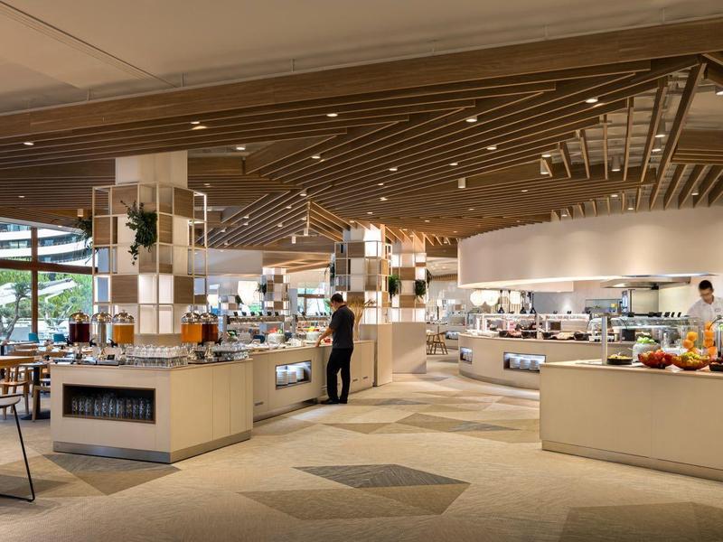 Moderne Kantine mit hellen Theken, Sitzplätzen und großen Fenstern, freundliche Atmosphäre.