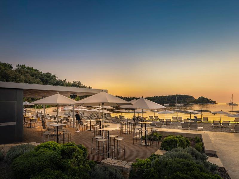 Strandterrasse mit Tischen, Sonnenschirmen und Stühlen bei Sonnenuntergang am Meer.