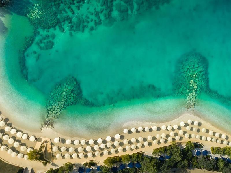 Luftaufnahme eines Strandes mit türkisfarbenem Wasser und Reihen von weißen Sonnenschirmen.