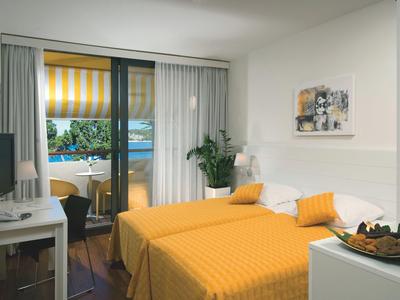 Hotelkamer met geel bed, bureau en balkon met uitzicht op zee.