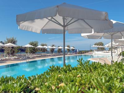 Großer Pool mit weißen Sonnenschirmen, grünen Pflanzen im Vordergrund und blauem Himmel.