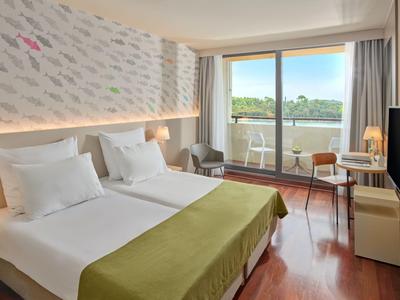 Modernes Hotelzimmer mit zwei Betten, Balkon und Aussicht auf grüne Landschaft.