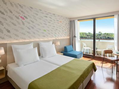 Modernes Hotelzimmer mit zwei Betten, Sitzbereich und Balkon mit Blick auf Grünflächen.