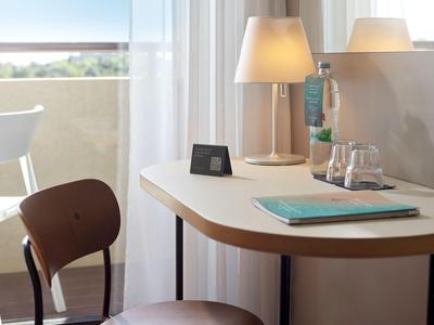 Moderner Hotelarbeitsplatz mit hellem Schreibtisch, Stuhl, Lampe und Blick auf Balkon und Meer.