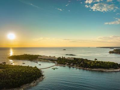 Insel mit üppiger Vegetation und Ufer bei Sonnenuntergang über ruhigem Meer.