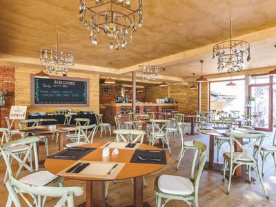 Licht restaurant met houten tafels, stoelen en kroonluchters, gezellige sfeer.
