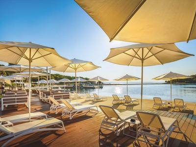 Zonnig terras met ligstoelen en parasols aan het water met uitzicht op eilanden.