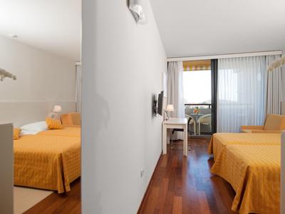 Moderní hotelový pokoj se dvěma oranžovými postelemi a přístupem na balkon přes skleněné dveře.