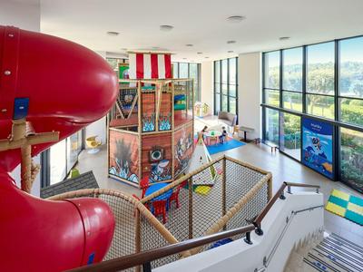 Blick auf ein modernes Hotelinnenspielzimmer mit großer roter Rutsche und Sitzgelegenheiten mit Panoramafenstern.