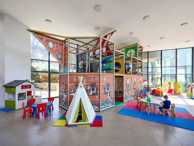 Moderner, heller Kinderspielraum mit Klettergerüst, Zelt und bunten Teppichen in einem Hotel.