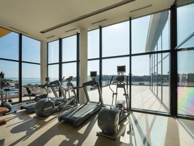 Fitnessraum mit modernen Geräten und großen Fenstern mit Ausblick auf die Stadt.