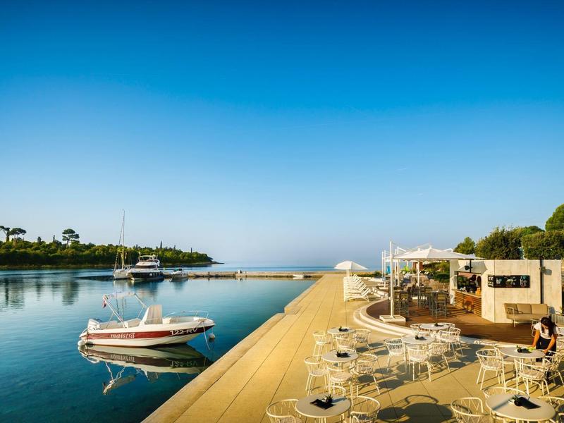 Slunečná scéna u vody s loděmi a venkovním posezením u klidné vody.