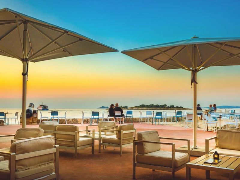 Venkovní posezení s deštníky s výhledem na pláž za západu slunce.