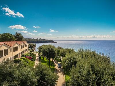 Ferienanlage mit Bungalows und Gartenwegen am Meer unter klarem blauen Himmel.