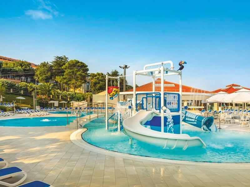 Großer Pool mit Wasserrutschen, Liegestühlen und Sonnenschirmen bei sonnigem Himmel.