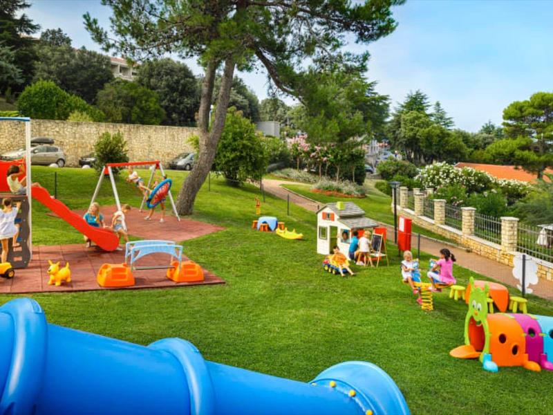 Kinderspielplatz mit Rutsche, Schaukeln, Klettergerüst und bunten Spielzeugen auf grünem Rasen.