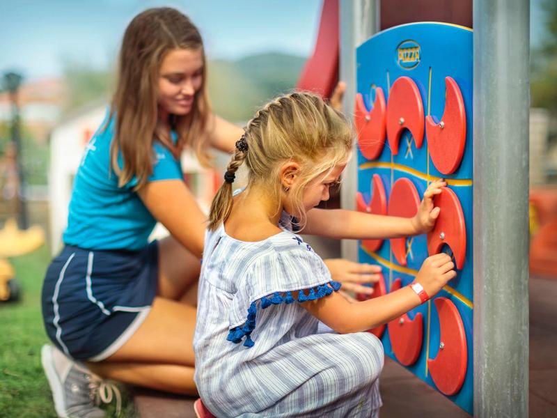 Zwei Mädchen spielen draußen an einer bunten, interaktiven Spielfläche auf einem Spielplatz.