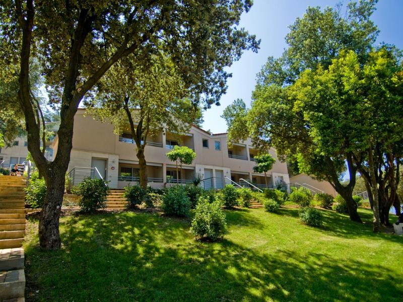 Ein großes Haus mit Terrassen, umgeben von Bäumen und grünem, sonnigem Garten.