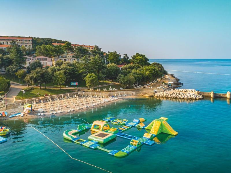 Klarer blauer Meeresblick mit aufblasbarem Wasserspielplatz nahe Küste und grünen Hügeln.