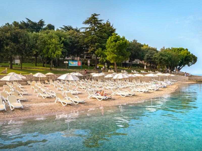 Ein leerer Sandstrand mit weißen Liegestühlen, Sonnenschirmen und klarem, blauem Wasser.