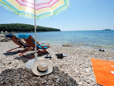 Spiaggia di ciottoli con sdraio, ombrellone e vista sul mare sotto un cielo limpido.
