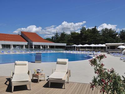 Großer Hotelpool mit Liegestühlen und Sonnenschirmen unter blauem Himmel.