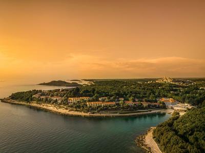 Küstenlandschaft mit Hotels und Wäldern unter orangefarbenem Himmel bei Sonnenuntergang.