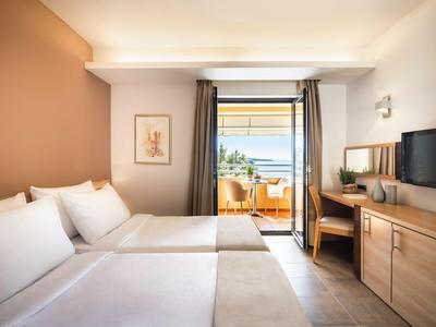 Hotelzimmer mit zwei Betten, Balkon und Blick auf das Meer bei klarem Wetter.