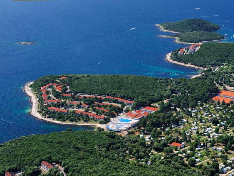 Veduta aerea di una località costiera circondata da foresta e mare blu.