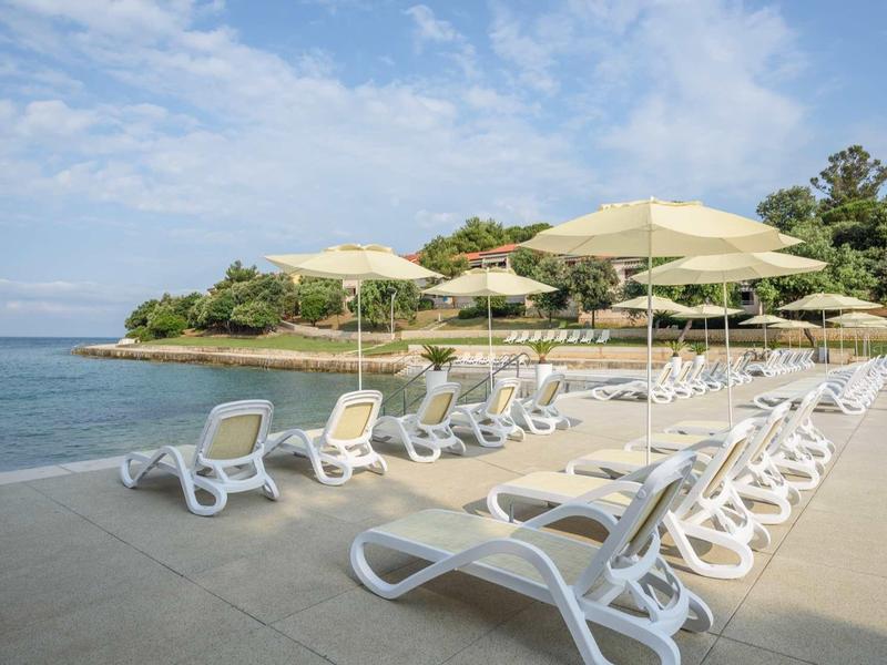 Area spiaggia con lettini bianchi e ombrelloni accanto al mare calmo sotto un cielo nuvoloso.