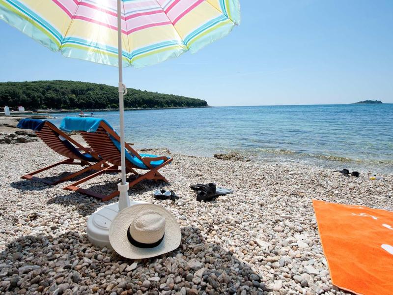 Spiaggia di ciottoli con sdraio, ombrellone e vista sul mare sotto un cielo limpido.
