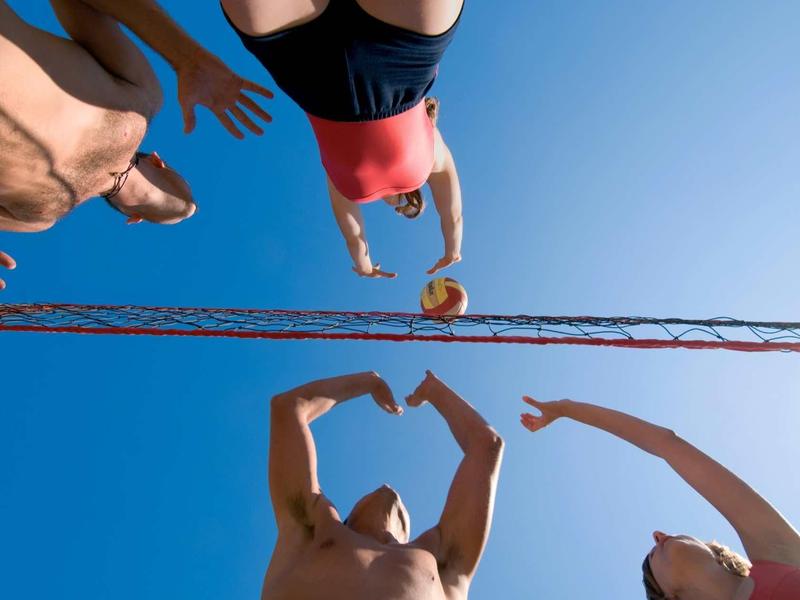 Persone che giocano a beach volley sotto un cielo azzurro, vista dal basso.