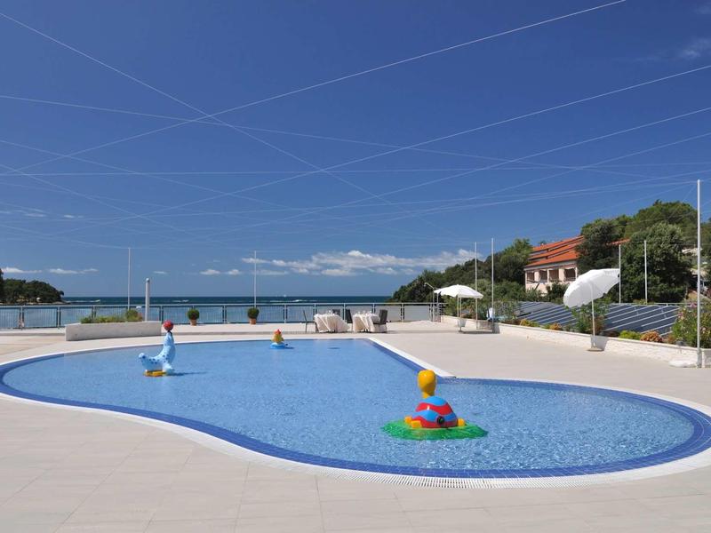 Piscina con attrazioni d'acqua e lettini vicino al mare sotto un cielo sereno