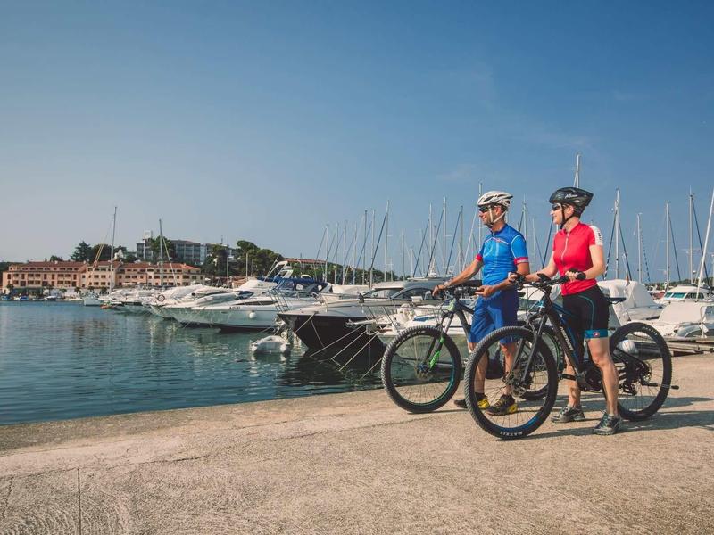 Due ciclisti con caschi sono fermi in un porto turistico sotto un cielo sereno.