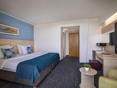 Modern eingerichtetes Hotelzimmer mit Doppelbett, Schreibtisch und Sitzbereich in neutralen Farben.