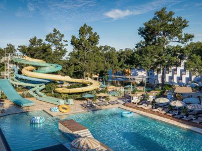 Poolbereich mit Wasserrutschen, Liegestühlen und Sonnenschirmen an einem sonnigen Tag.